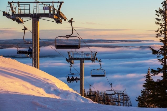 Ski lift over snowy mountains above the clouds in Tsaghkadzor, Armenia during winter sunset.