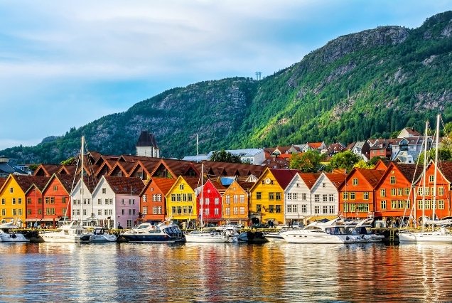 Colorful historic wooden buildings of Bryggen at Bergen harbor, Norway, under a blue sky with green mountain backdrop.