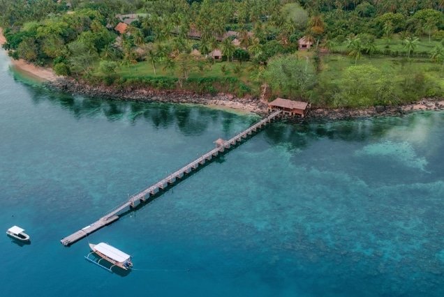 Long wooden pier extending into clear turquoise water at a tropical coastal resort in Lombok, Indonesia.