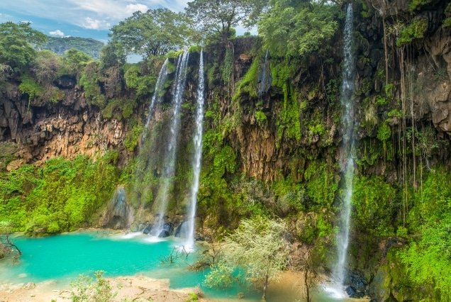 Lush green waterfall in Salalah, Oman, during Khareef season; travel guide for Oman e-visa services from Dubai, UAE.